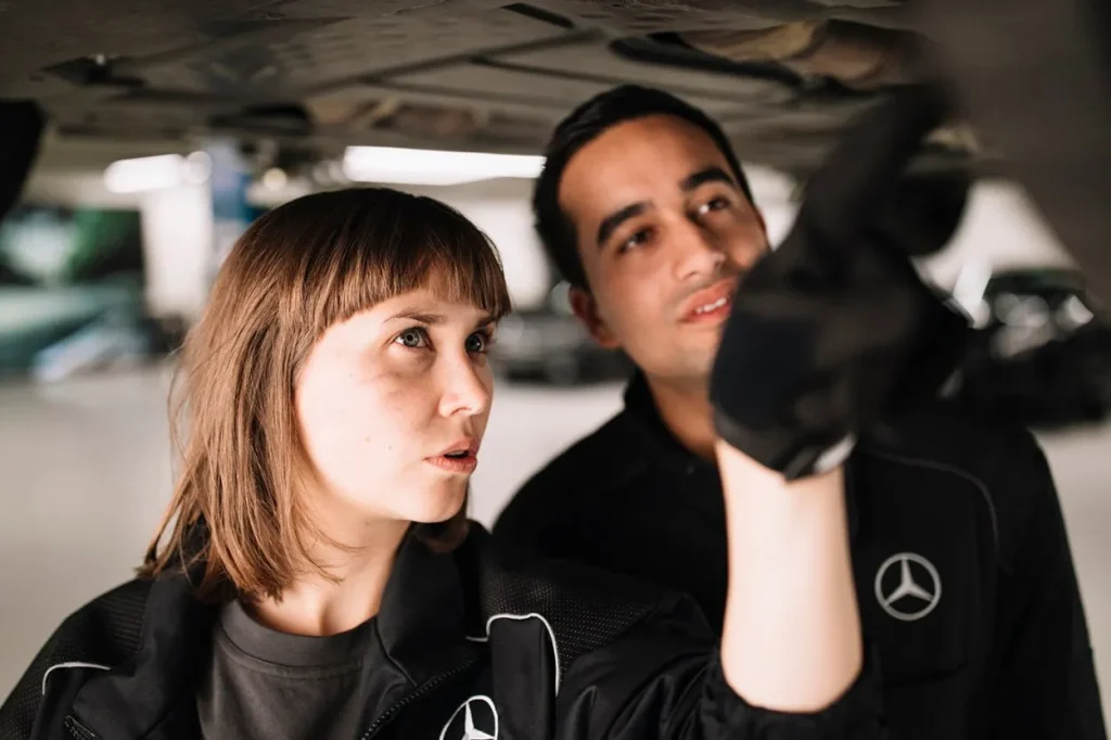 Zwei Fahrzeugbaumechaniker inspezieren den boden eines Fahrzeuges unter einer Hebebühne