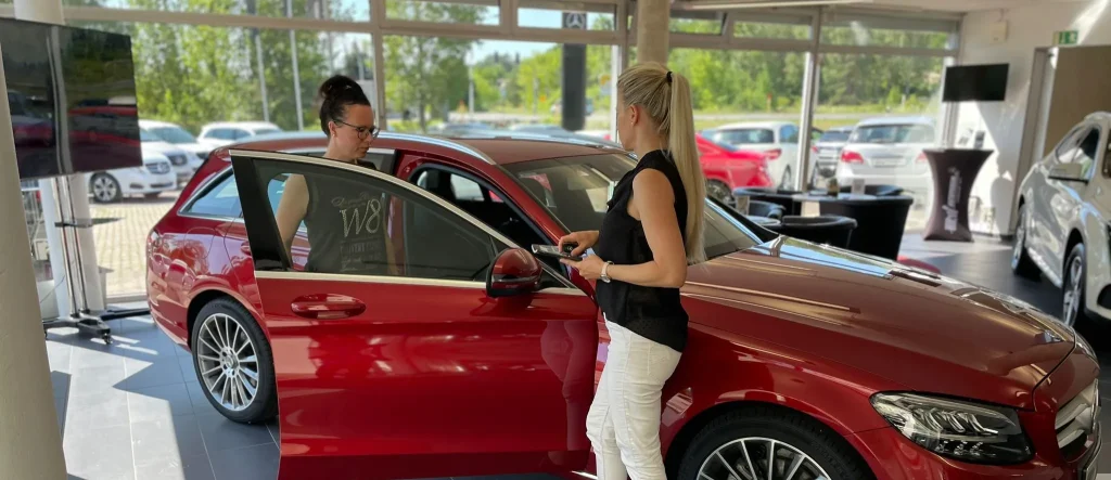 Frau Peitzer zeigt einer Kundin im Autohaus einen roten Mercedes.