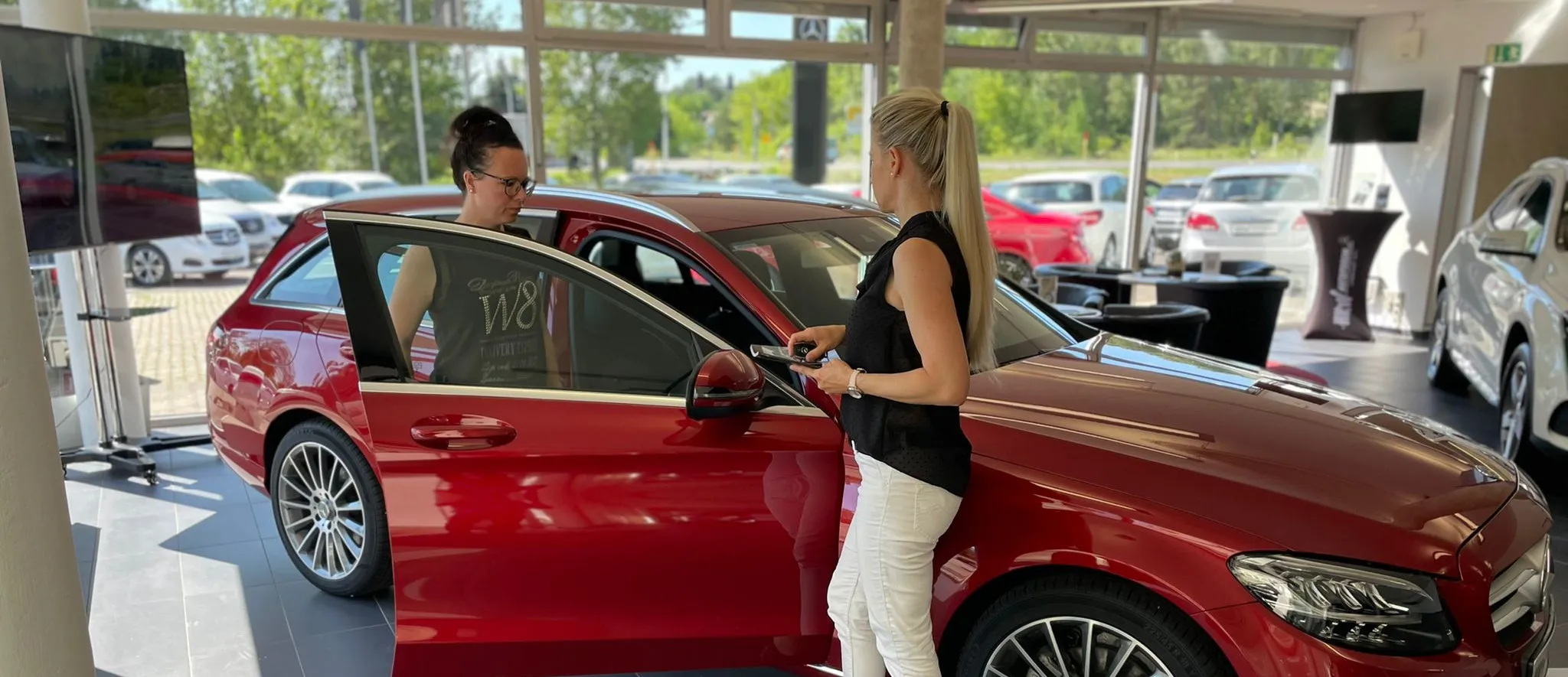 Frau Peitzer zeigt einer Kundin im Autohaus einen roten Mercedes.